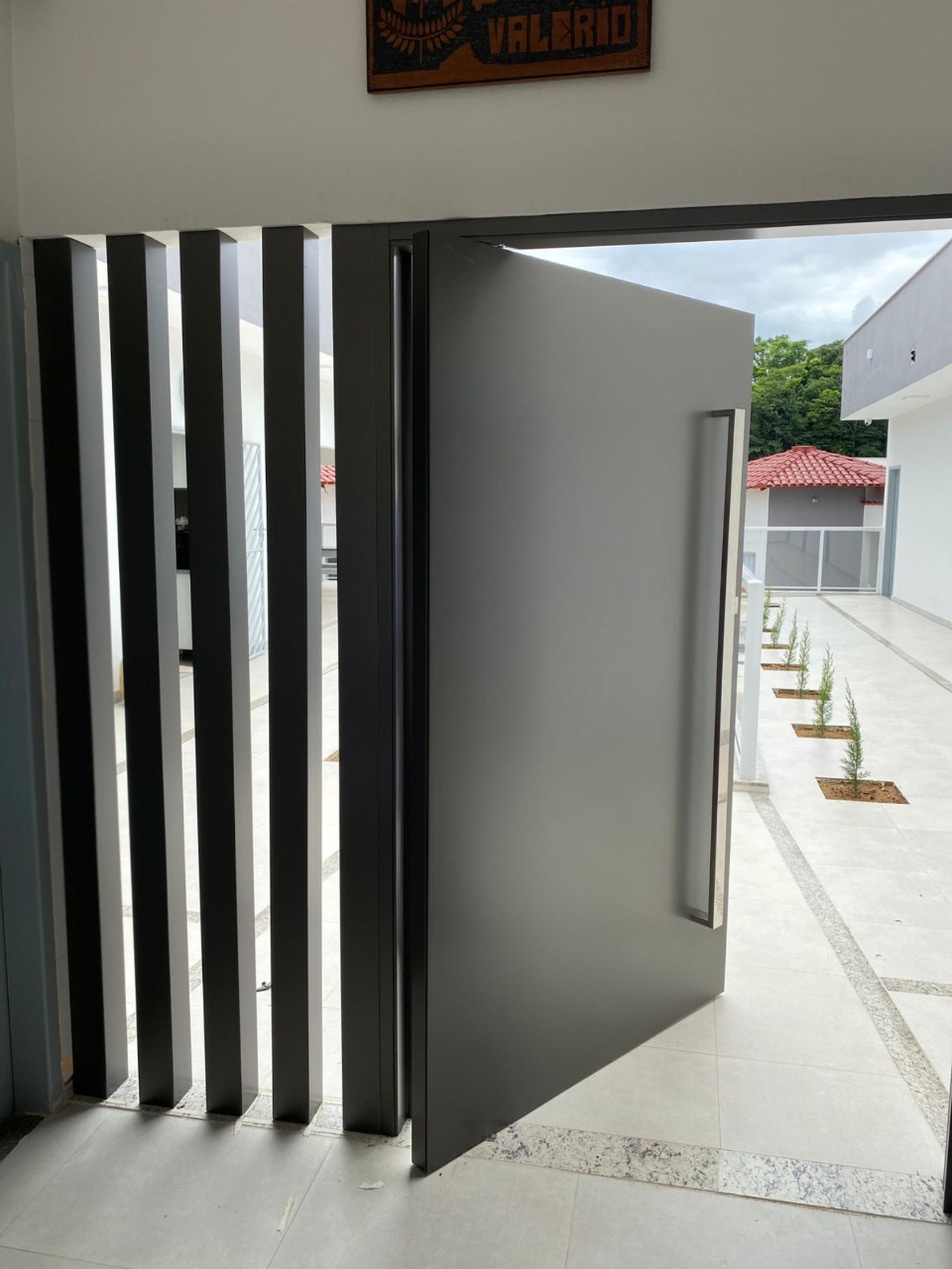 Porta pivotante em ACM preto com detalhe lateral em ripas metálicas, instalada pela Giga Projetos.
