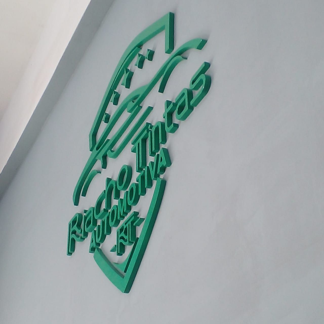 Logomarca Riacho Tintas em letras caixa verdes aplicadas em parede cinza produzida pela Giga Projetos.